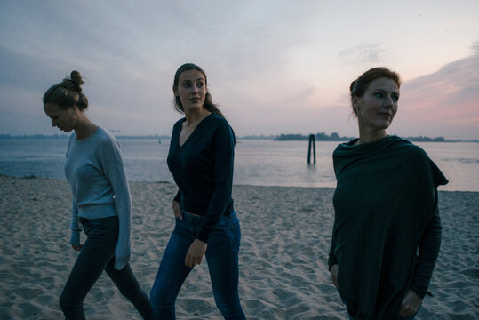 Germany, Hamburg, mother with two teenage girls walking on the beach at Elbe shore in the evening