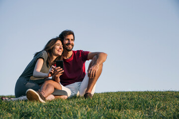 Naklejka na ściany i meble Couple sitting on grass against clear sky during sunset