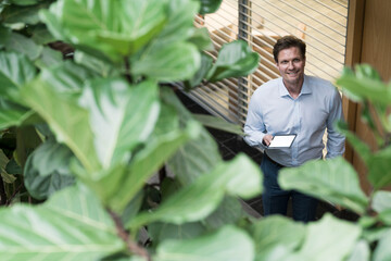 Businessman standing in sustainable office building, holding digital tablet