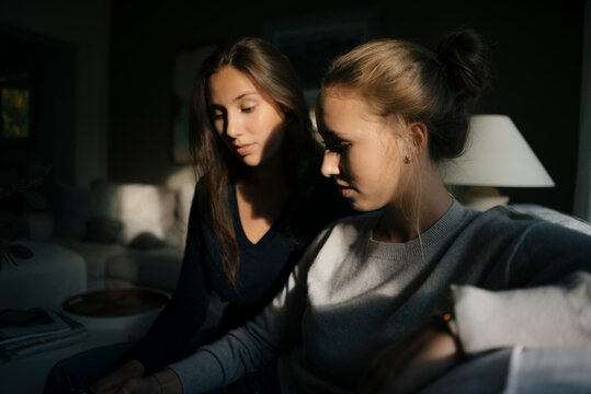 Two teenage girls using cell phone on couch at home