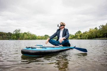 Foto op Canvas Businessman wearing VR glasses sitting on SUP board on a lake © Joseffson/Westend61