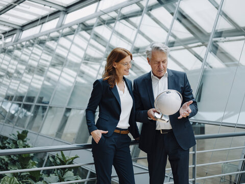 Businessman and businesswoman looking at globe in modern office building