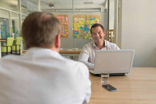 Two businessmen with laptop talking in office