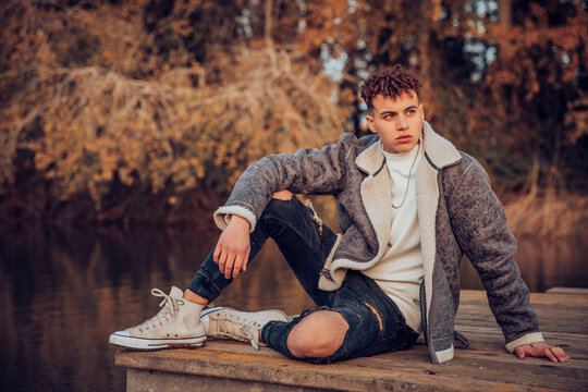 Young man wearing jacket sitting on jetty against lake at autumn forest