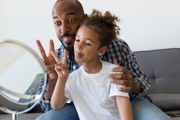 Father and daughter at home pulling funny faces and looking in mirror