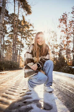 Young woman crouching on snowy road at park during sunny day