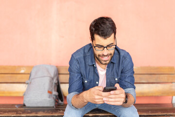 Portrait of smiling man sitting on wooden bench using smartphone