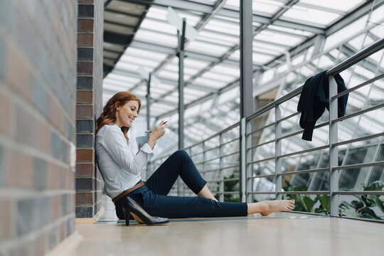 Businesswoman sitting on the floor in office eating muesli