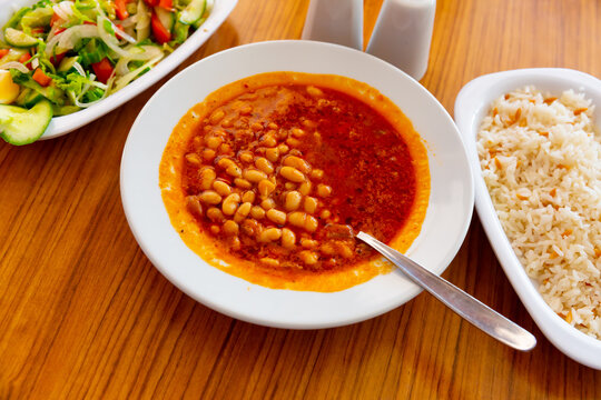 Traditional Turkish Kuru fasulye, spicy stewed bean dish in tomato sauce served with rice and fresh vegetable salad