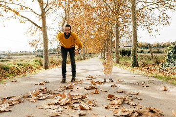 Father and daughter playing on a way in the park in autumn