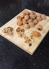 Whole and cracked walnuts on a wooden board. On a black marble table. Copy space.