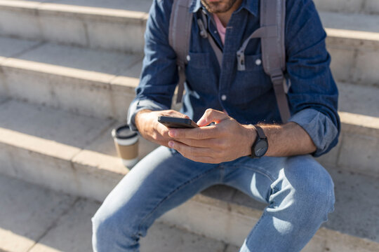 Crop view of man sitting on stairs using smartphone