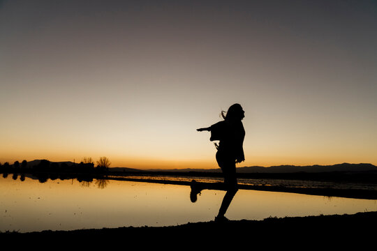 Young woman twirling on one leg during sunset at Ebro Delta, Spain