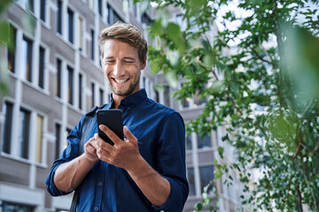 Happy young businessman using mobile phone in the city