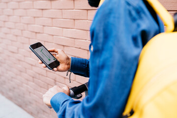 Man with backpack and E-Scooter using navigation app on his mobile phone, partial view