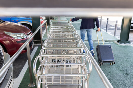 Crop view of man pulling trolley bag walking along row of baggage carts