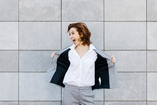 Portrait of a screaming young businesswoman in front of wall with gray tiles, opening her jacket