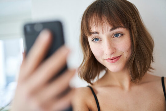 Portrait of smiling young woman taking selfie with smartphone at home