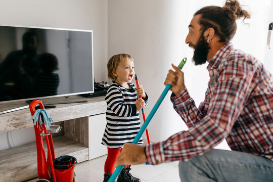 Father and little daughter having fun together while cleaning the living room