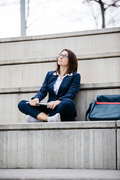 Businesswoman sitting outdoors on stairs with laptop looking up