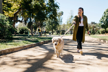 Happy woman going walkies in city park with her Labrador Retriever