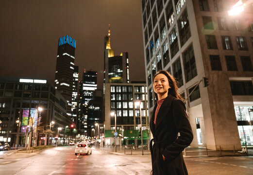 Young woman crossing the street in the city at night, Frankfurt, Germany