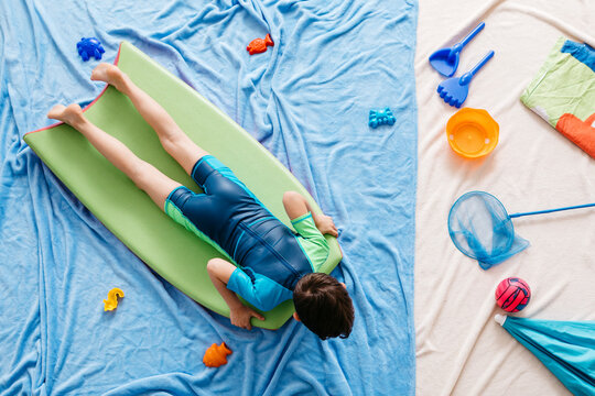 Boy lying on swimming board floating in water, beach equipment at the beach