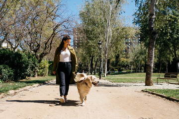 Happy woman going walkies in city park with her Labrador Retriever