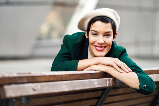 Portrait of smiling fashionable young woman sitting on a bench