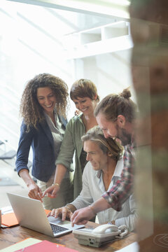 Smiling team of employees working on laptop while standing in office