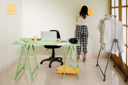 Young woman standing in office at a wall taking notes on adhesive notes
