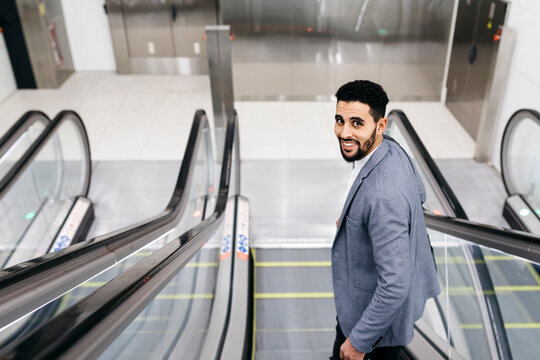 Portrait of smiling young businessman on escalator turning round