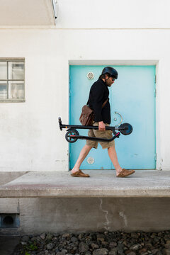 Man wearing cycling helmet carrying folded Electric Scooter
