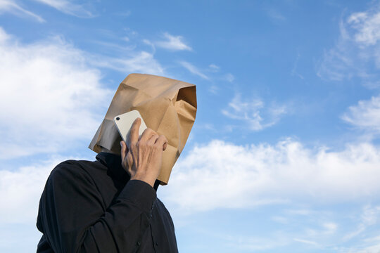 Man with paper bag above his head talking on cell phone