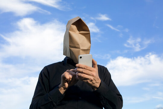 Man with paper bag above his head using cell phone