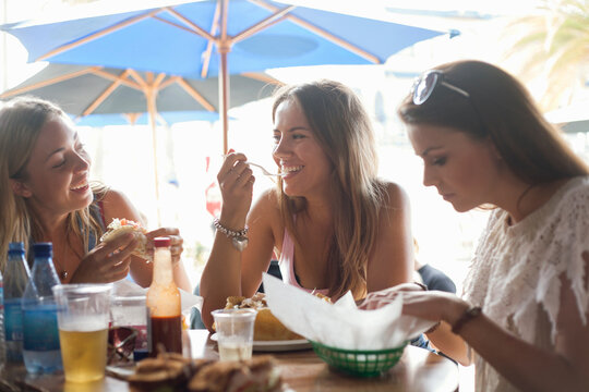 Happy female friends having lunch at beach restaurant during vacation