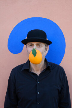 Portrait of man with an orange at a wall with question mark wearing a bowler hat
