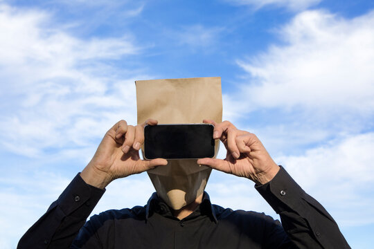 Man with paper bag above his head using cell phone