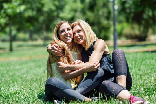 Sportive mature woman and her daughter embracing on a meadow in a park