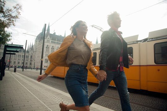 Happy woman holding hands with male partner while running in city