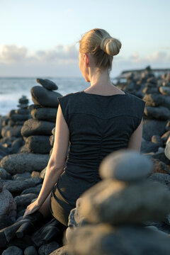 Spain, Tenerife, Costa Adeje, woman sitting between cairns at the coast