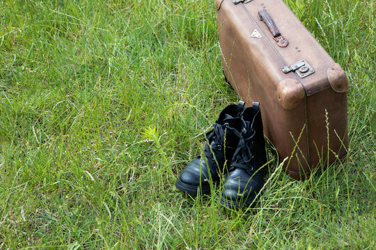 Old brown leather suitcase and pair of black boots on a meadow