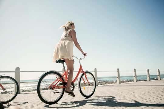 Young woman cycling on promenade against clear sky on sunny day