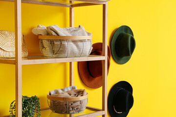 Modern organizers with clothes on shelf near yellow wall
