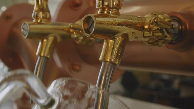 Tilt down on barman pulling a pint of foamy beer on a vintage brass and golden beer tap