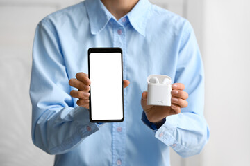 Woman holding modern mobile phone and earphones on light background