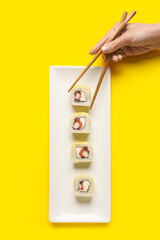 Woman taking delicious sushi roll from plate on yellow background