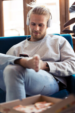 Young man sitting on couch with cell phone and headphones