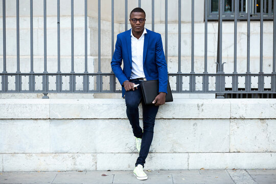 Young businessman wearing blue suit jacket and holding smartphone and laptop bag