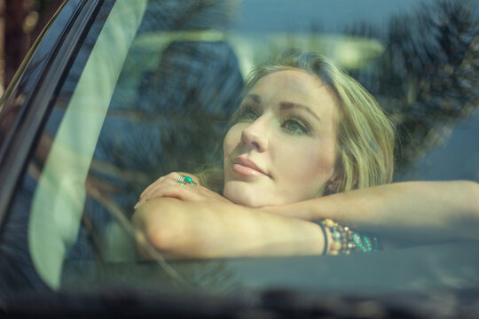 Thoughtful woman with arms crossed leaning inside car on windshield